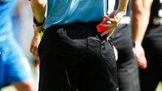 Ein Schiedsrichter zieht in einem Fußballspiel die rote Karte aus seiner Gesäßtasche.