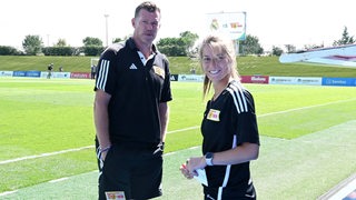 Der U19-Trainer Marco Grote von Union Berlin steht neben seiner strahlenden Co-Trainerin Marie-Louise Eta am Rande des Trainingsplatzes.