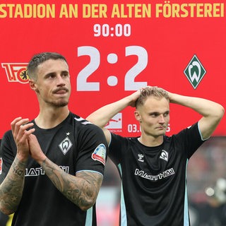 Werder-Kapitän Marco Friedl applaudiert, während Amos Pieper die Hände hinter dem Kopf verschränkt. 