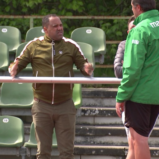 Ailton schaut bei einem Fußball-Spiel von Werders U23 zu und steht am Zaun.