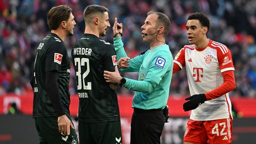Im Spiel zwischen Bayern München und Werder Bremen diskutieren Werder-Spieler um Kapitän Marco Friedl mit dem Schiedsrichter.