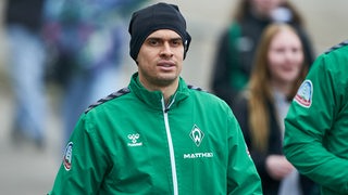Werder-Stürmer Rafael Borré mit einer schwarzen Mütze und in grüner Trainingsjacke auf dem Weg zum Trainingsplatz.