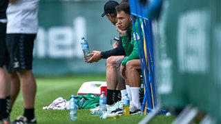 Werder-Spieler Lee Buchanan sitzt am Rande des Trainings nachdenklich auf der Ersatzbank.