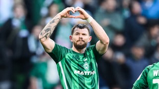 Werder-Stürmer Oliver Burke formt nach einem Spiel mit seinen Händen ein Herz und dreht sich in Richtung der Werder-Fans.