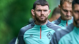 Werder-Stürmer Oliver Burke geht mit seinen Mitspielern und ernster Miene zum Trainingsplatz.
