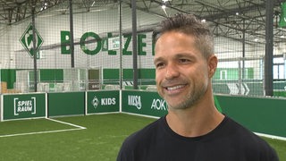 Werders ehemaliger Spieler Diego steht lächelnd in Werders Fußballhalle bei einem Interview.
