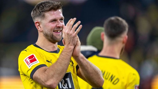 Fußballer Niclas Füllkrug von Borussia Dortmund applaudiert mit verschmitztem Grinsen den Fans nach dem Spiel, seine markante Zahnlücke blitzt dabei auf.