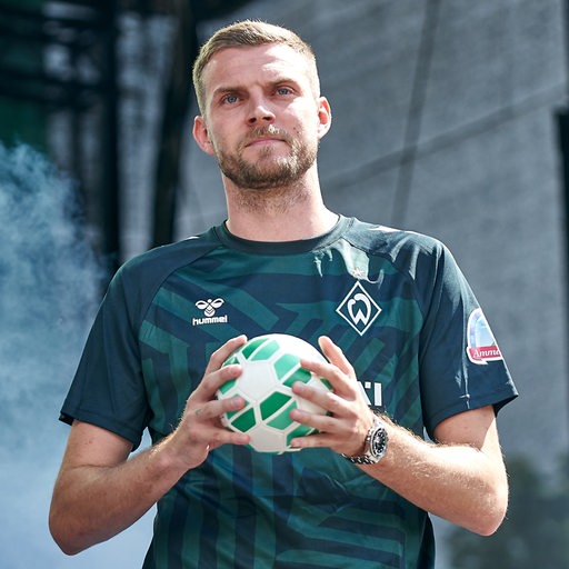 Werder-Stürmer Marvin Ducksch steht bei der Mannschaftsvorstellung nachdenklich mit Ball in der Hand auf der Bühne.