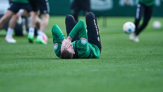 Werder-Stürmer Marvin Ducksch hält sich während des Trainings auf dem Rücken liegend mit sichtlichen Schmerzen die Hände vors Gesicht.