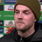 Werder-Stürmer Marvin Ducksch trägt eine dunkelgrüne Wollmütze und steht nach einem Spiel vor einer Werbewand beim Interview.