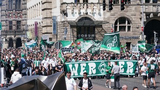Das Foto zeigt viele Werder-Fans, die gemeinsam mit einem Banner, vielen Fahnen und Transparenten durch Bremen laufen.