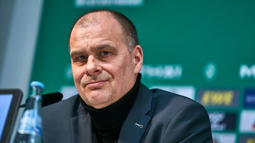Werders Finanzchef Klaus Filbry lächelt auf dem Podium einer Pressekonferenz.
