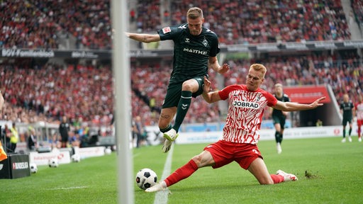 Werder-Stürmer Marvin Ducksch springt an der Seitenlinie hoch, während ihm sein Freiburger Gegenspieler den Ball weggrätscht.
