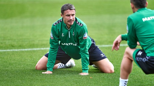Werder-Kapitän Marco Friedl knien während des Trainings auf dem Rasen.