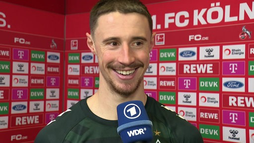 Werder-Kapitän Marco Friedl gut gelaunt beim Interview nach dem Köln-Sieg vor einer Werbewand.