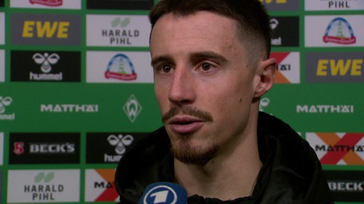 Werder-Kapitän Marco Friedl steht nach der Niederlage gegen Gladbach vor einer Werbewand bei einem Interview.
