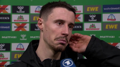 Werder-Kapitän Marco Friedl schaut enttäuscht beim Interview vor einer Werbewand nach der Niederlage gegen Heidenheim.