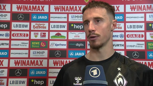 Werders Kapitän Marco Friedl steht nach dem Sieg in Stuttgart vor einer Werbewand beim Interview.