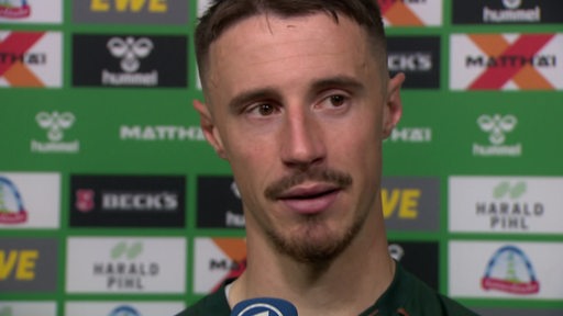Werder-Kapitän Marco Friedl steht nach dem Spiel gegen Leipzig vor einer Werbewand beim Interview.