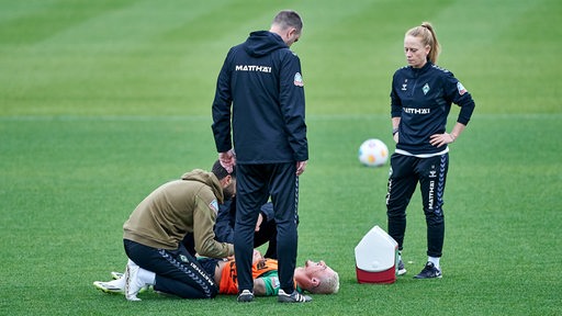 Werder-Kapitän Marco Friedl liegt während des Trainings rücklings auf dem Rasen und wird behandelt, Trainer Ole Werner schaut zu.