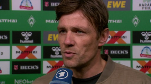 Werder-Sportchef Clemens Fritz steht nach einem Spiel vor einer Werbewand beim Interview.
