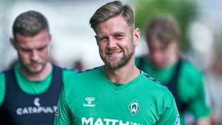 Werder-Stürmer Niclas Füllkrug mit verschmitztem Grinsen auf dem Weg mit der Mannschaft zum Trainingsplatz.
