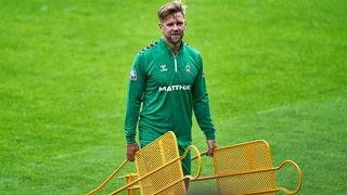 Werder-Stürmer Niklas Füllkrug trägt nach dem Training zwei gelben Metallmännchen vom Platz.