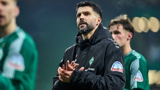 Werder-Verteidiger Anthony Jung applaudiert nach dem Spiel mit seinen Teamkollegen den Fans und trägt dabei schon die schwarze Wintertrainingsjacke.