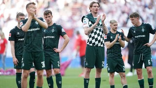 Werder-Spieler um Nick Woltemade stehen nachdenklich nach dem Spiel auf dem Rasen und applaudieren den mitgereisten Fans in Leipzig.