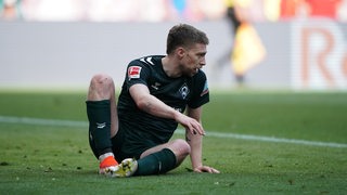 Werder-Profi Mitchell Weiser sitzt in Spiel gegen Leipzig auf dem Rasen und will wieder aufstehen.