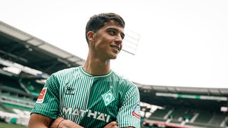 Werder-Neuzugang Julian Malatini posiert lächelnd im Weser-Stadion im Werder-Trikot.