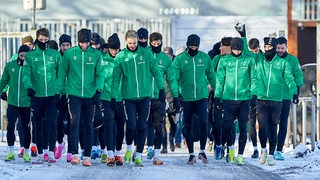 Werder-Spieler sind als Gruppe gemeinsam auf dem verschneiten Weg zum Trainingsplatz.