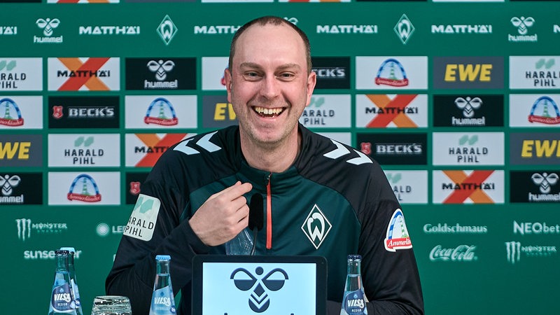 Ole Werner sitzt lachend bei einer Pressekonferenz