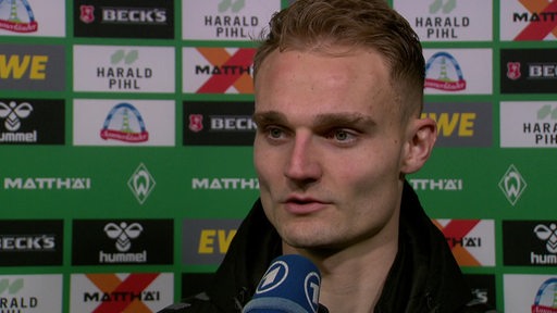 Werder-Profi Amos Pieper steht nach einem Spiel vor einer Werbewand beim Interview.