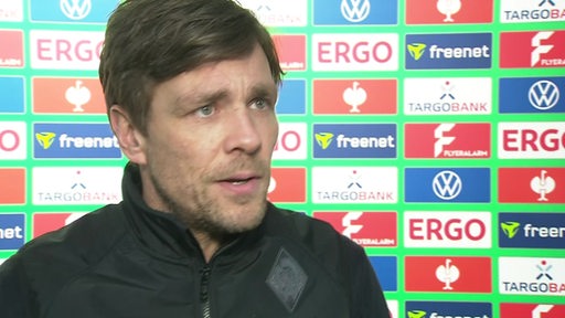 Werders Sportchef Clemens Fritz steht nach dem Pokal-Aus in Bielefeld vor einer Werbewand beim Interview.