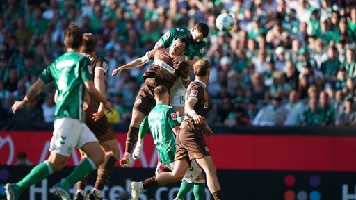 Fußballspieler von Werder Bremen tummeln sich bei einem Eckball im Strafraum mit Gegenspielern von Sankt Pauli, ein Werder-Spieler steigt im Getümmel zum Kopfball hoch.