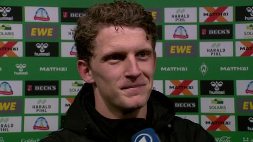 Werder-Torschütze Jens Stage lächelnd nach dem Spiel gegen Stuttgart vor einer Werbewand beim Interview.
