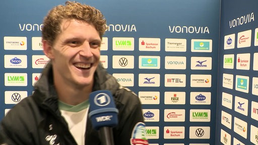 Werder-Torschütze Jens Stage steht lächelnd nach dem Spiel in Bochum vor einer Werbewand beim Interview.