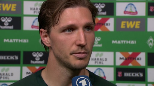 Werder-Profi Niklas Stark steht nach dem Spiel gegen Leipzig vor einer Werbewand beim Interview.