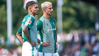 Werder-Kapitän Marco Friedl und Justin Njinmah stehen nachdenklich nach dem Testspiel in Verden nebeneinander auf dem Spielfeld.