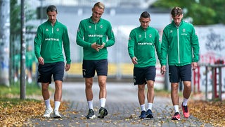 Werder-Spieler Marco Friedl, Amos Pieper, Rafael Borré und Olivier Deman laufen nebeneinander den Weg zum Trainingsplatz entlang.