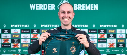 Ole Werner hält das neue Werder-Trikot in der Hand