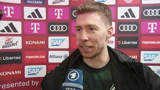 Werder-Spieler Mitchell Weiser lächelt beim Interview vor einer Werbewand nach dem Sieg gegen Bayern München.