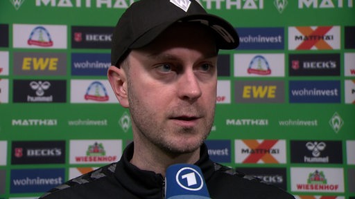 Werder-Trainer Ole Werner steht nach der Niederlage gegen Heidenheim vor einer grünen Werbewand beim Interview.