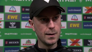 Werder-Trainer Ole Werner steht nach dem Remis gegen Darmstadt vor einer grünen Werbewand beim Interview.