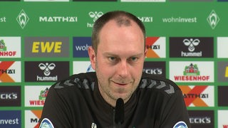 Werder-Trainer Ole Werner lächelt während einer Pressekonferenz.