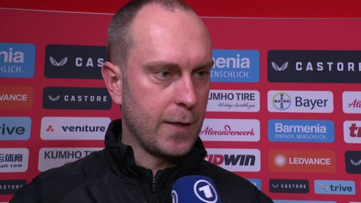 Werder-Trainer Ole Werner steht nach der Niederlage gegen Levekusen vor einer Werbewand beim Interview.