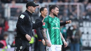Werder-Trainer Ole Werner steht bei einem Spiel an der Seitenlinie und hat die Hand auf die Schulter von Stürmer Oliver Burke gelegt, der gerade eingewechselt werden soll.