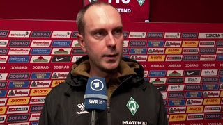 Werder-Trainer Ole Werner vor einer Werbewand beim Interview nach dem Spiel in Freiburg.