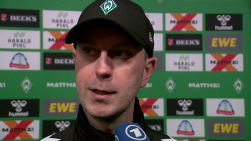 Werder-Trainer Ole Werner steht nach der Niederlage gegen Gladbach vor einer Werbewand beim Interview.